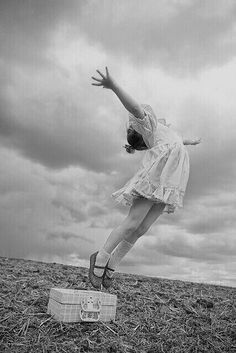 a woman is jumping in the air with her arms outstretched and suitcase on the ground