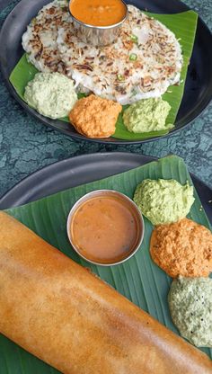 two plates filled with food on top of a green leaf covered table next to a bowl of dipping sauce