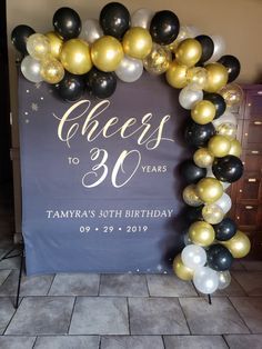 a balloon arch that says cheers to 30 years with black, white and gold balloons