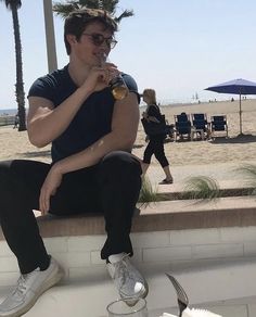 a man sitting on a ledge drinking from a bottle and holding a drink in his hand