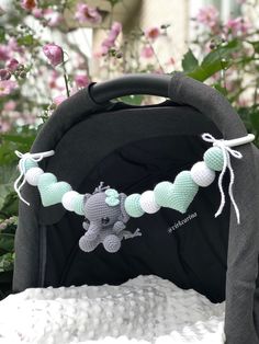 a crocheted teddy bear is attached to a stroller in front of flowers