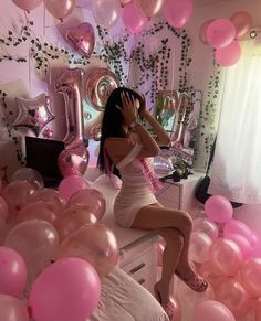 a woman sitting on top of a bed surrounded by pink and white balloons in the air