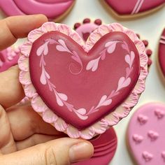 a hand holding a heart shaped cookie in front of pink and white decorated sugar cookies