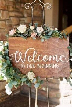 a welcome sign with flowers and greenery on it is standing in front of a brick wall