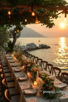 an outdoor dining table set up with candles and flowers on it, overlooking the ocean