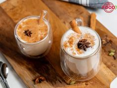 two glasses of hot chocolate on a wooden cutting board with spoons and cinnamon sticks