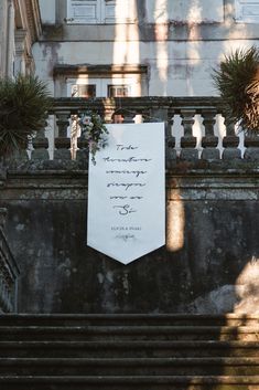 a white sign hanging from the side of a building next to some planters and stairs