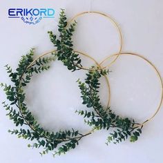 three gold hoop wreaths with green leaves hanging from the sides on a white wall