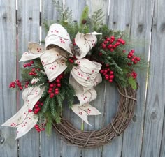 a wreath with red berries and evergreens on it hanging on a wooden fence outside