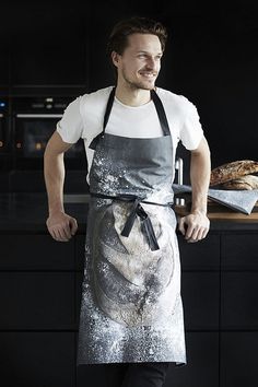 a man wearing an apron standing in front of a counter top with bread on it