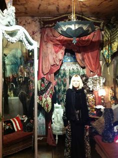 a woman standing in front of a mirror with lots of clothes hanging on the walls