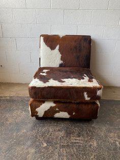 a brown and white cowhide chair against a brick wall