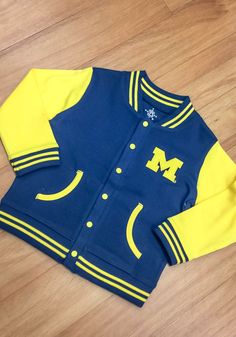 Michigan Wolverines Toddler Navy Blue Varsity Outerwear Light Weight Jacket Team-colored Outerwear With Team Name For Game Day, Collegiate Outerwear With Team Name For Game Day, Team-colored Outerwear For Game Day With Team Spirit, Team-colored Outerwear For Game Day, Team-colored Outerwear For Game Day And Sports Season, Blue Sporty Outerwear For Game Day, Long Sleeve Outerwear With Ribbed Cuffs For Game Day, Game Day Outerwear With Ribbed Cuffs For Sports Season, Collegiate Outerwear With Ribbed Cuffs For School