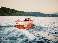 two people are riding in a speedboat on the water with an american flag flying