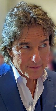 a close up of a person wearing a blue suit and white shirt with his eyes open