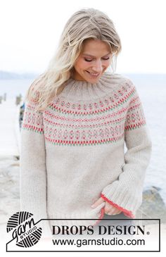 a woman standing on the beach with her hands in her pockets and wearing a sweater