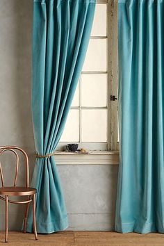 a room with a chair, window and blue curtained drapes on the windowsill