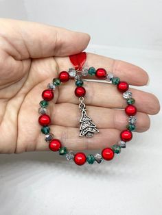 a woman's hand holding a red beaded bracelet with a christmas tree charm