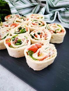 several rolls filled with meat and veggies on top of a black cutting board