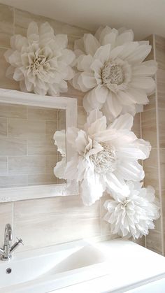 a white sink sitting under a mirror next to a wall with flowers on the wall