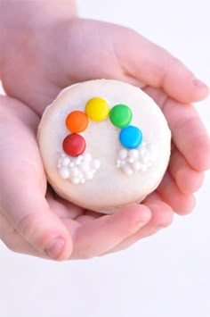 a person holding a small white cookie with candy on it's top and the words rainbow macarons written below