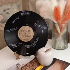 a record with writing on it sitting next to a vase filled with flowers and feathers