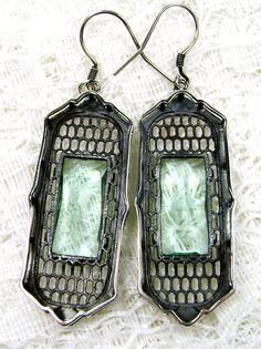 pair of earrings with green glass in the center on white lace fabric, closeup