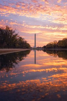 the washington monument at sunset with clouds reflected in it's water and trees around it