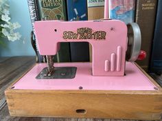 an old pink sewing machine sitting on top of a wooden box next to some books