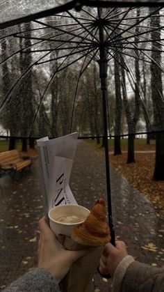 a person holding an umbrella over a cup of coffee and croissant in the rain