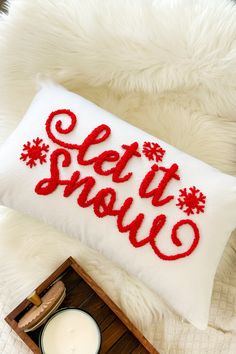 a white pillow with red lettering on it sitting next to a candle and a wooden tray