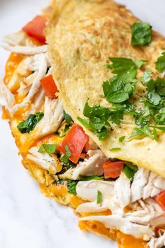 an omelet filled with chicken, tomatoes and parsley on top of a white plate