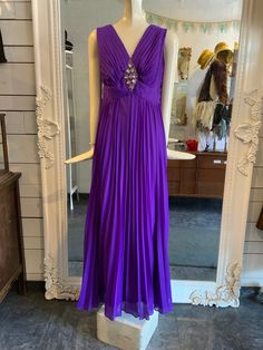 "Stunning purple pleated maxi dress with a fabulous beaded appliqué just under the neckline. The cut of the waist is a touch higher and is very flattering, giving it a bit of a princess cut/vibe. The skirt has quite a bit of fabric and moves beautifully as you walk or dance!  Lined. Does up with a zipper down the back. Condition: Great - there is a hook and eye on the back, at the top of the zipper- the \"eye\" portion is no longer there. Label: a Melody dress Fabric Content: no fabric label, but is likely polyester and acetate Size on Label: none Measurements: Shoulder to shoulder: approx 15\" Bust: 38\" Waist: 30\" Hip: 42\" Length: 56.5\"  Arm Opening: 15\" *IMPORTANT NOTE: All measurements are taken with the garment lying flat and then doubled. Please leave some wiggle room for comfort Pleated Floor-length Evening Dress For Prom, Floor-length Pleated Evening Dress For Prom, Purple Evening Gown With Pleated Bodice, Purple Maxi Dress For Party, Purple Maxi Dress For Prom Season, Purple Maxi Dress For Prom, Purple Floor-length Maxi Dress With Ruched Bodice, Fitted Purple Gown With Pleated Bodice, Elegant Purple Floor-length Maxi Dress