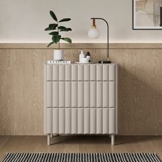 a white cabinet sitting next to a potted plant on top of a wooden floor