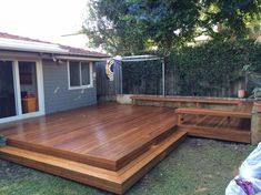 a large wooden deck in front of a house with trees and bushes around the back yard