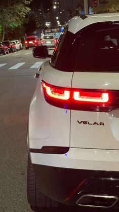 the rear end of a white car parked in front of a street with cars on it