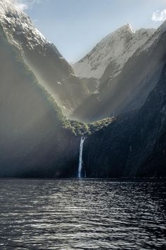 a waterfall in the middle of a mountain range with sunlight coming from behind it and water below