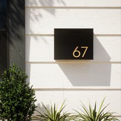 a house number sign mounted to the side of a white building with potted plants