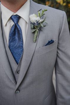 a man in a gray suit with a blue tie and flower boutonniere