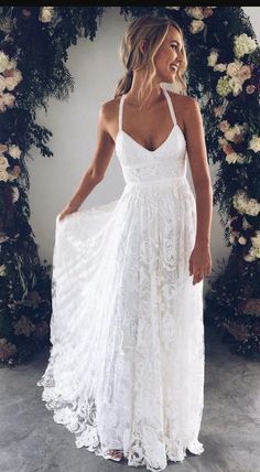 a woman wearing a white dress standing in front of a floral arch