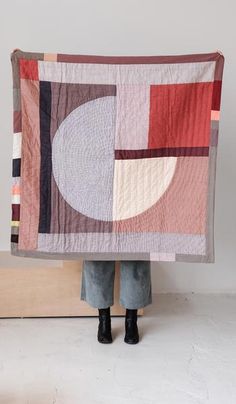 a woman is holding up a quilt that has been made with squares and circles on it