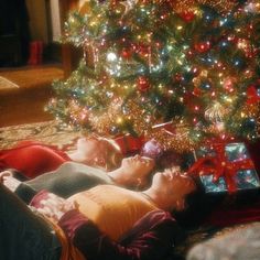 two people laying on the floor in front of a christmas tree