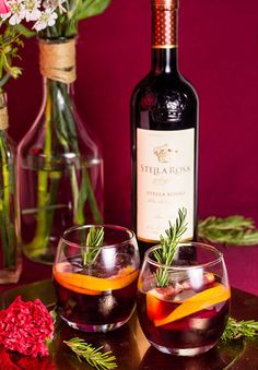 two glasses filled with wine and garnished with orange peels next to a bottle