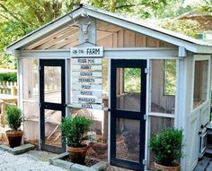 a small white chicken coop with black doors and windows on the side, surrounded by potted plants