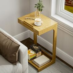 a small wooden table with books and a vase on it next to a white couch