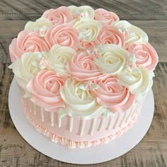 a cake decorated with pink and white frosting roses on top of a wooden table