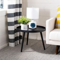 a small table with a potted plant on it next to a white chair and striped curtains