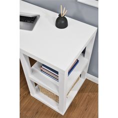 a white table with a black vase on top and bookshelves below the shelf