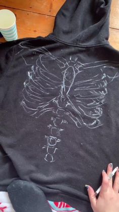 someone is drawing a skeleton on a black hoodie with white chalk and pencils