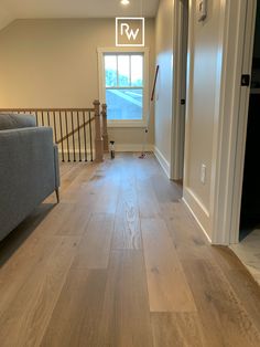 an empty living room with hard wood flooring and white walls, along with a gray couch